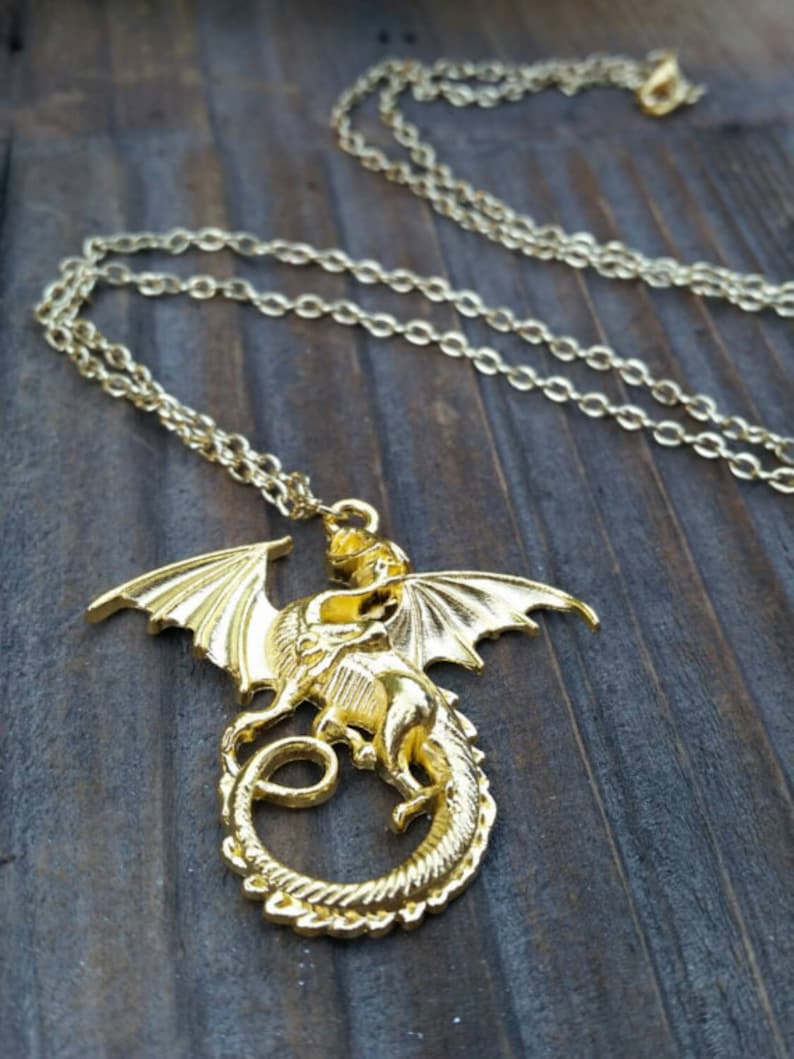 May include: A gold dragon pendant necklace with a detailed design. The dragon is curled up with its wings spread out. The necklace is on a gold chain.