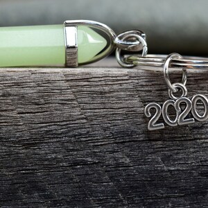 May include: A green crystal charm attached to a silver key ring with a 2020 charm hanging from it.