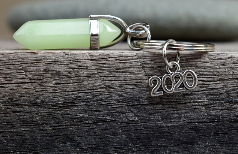 May include: A green crystal charm attached to a silver key ring with a 2020 charm hanging from it.