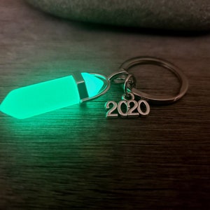 May include: A green glow-in-the-dark crystal charm attached to a silver key chain with a 2020 charm.