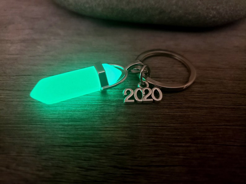 May include: A green glow-in-the-dark crystal charm attached to a silver key chain with a 2020 charm.