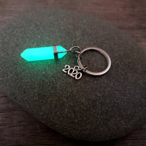 May include: A green glow-in-the-dark crystal keychain with a silver ring and the year 2020 attached.