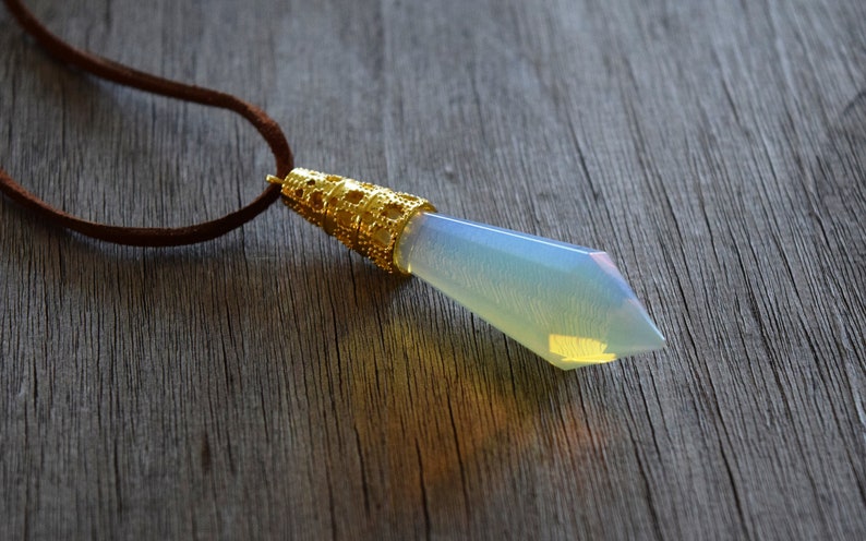 May include: A gold pendant with a clear iridescent gemstone in the shape of a teardrop. The pendant is attached to a brown leather cord.