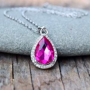Puede incluir: Un collar de plata con un colgante en forma de l&aacute;grima que presenta un gran cristal rosa brillante rodeado de cristales transparentes m&aacute;s peque&ntilde;os.