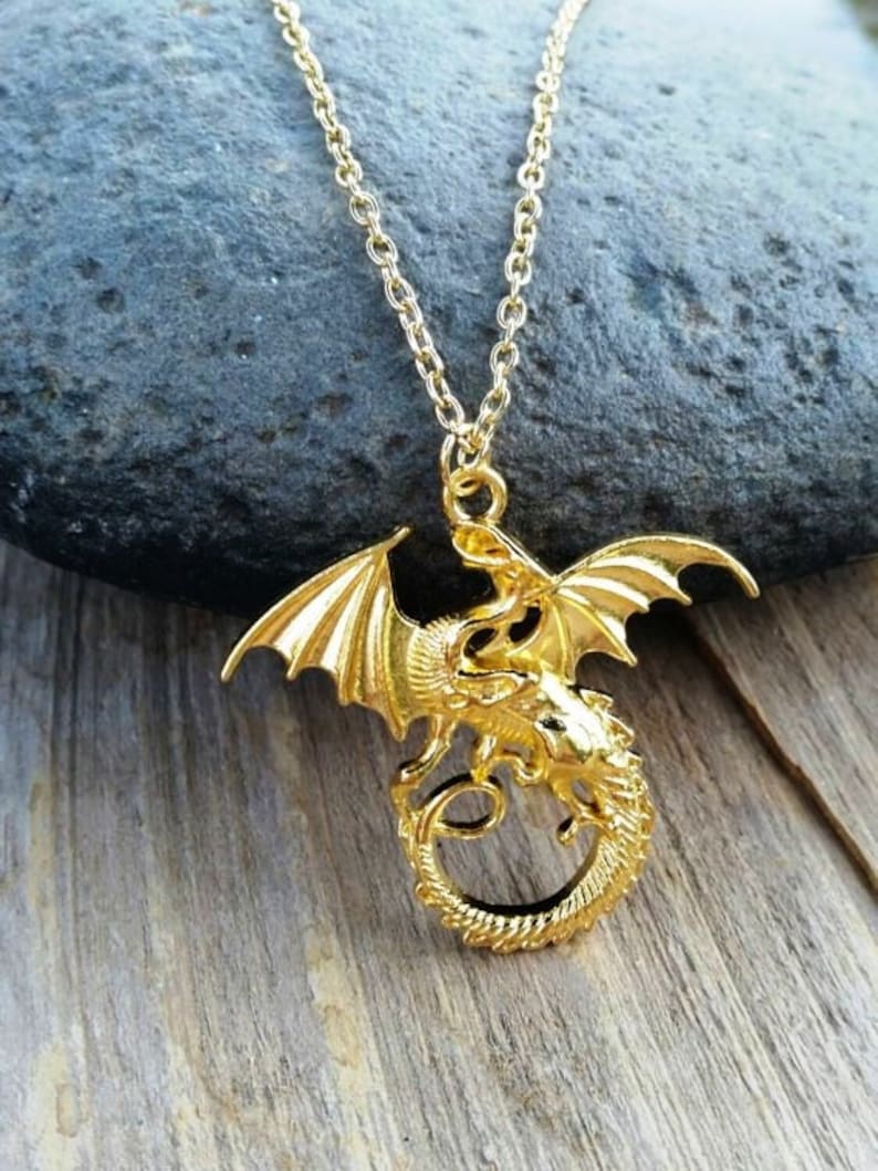 May include: A gold-toned dragon pendant necklace. The dragon is curled around itself with its wings spread out. The necklace is on a chain.
