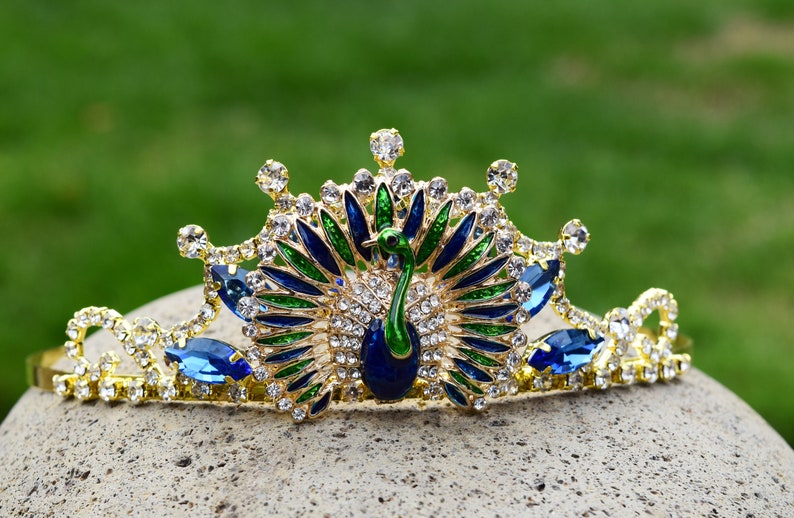 May include: A gold crown with blue and green peacock feathers and rhinestones.