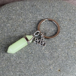 May include: A silver key chain with a light green crystal charm and a silver charm with the year 2020.