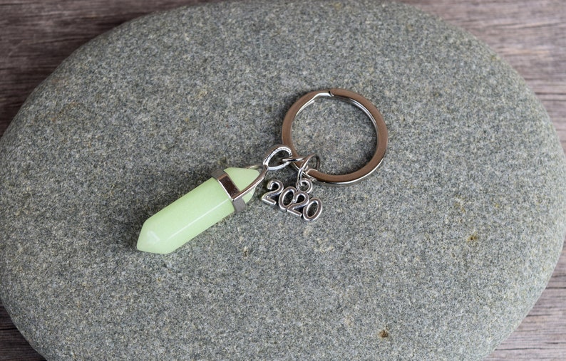 May include: A silver key chain with a light green crystal charm and a silver charm with the year 2020.