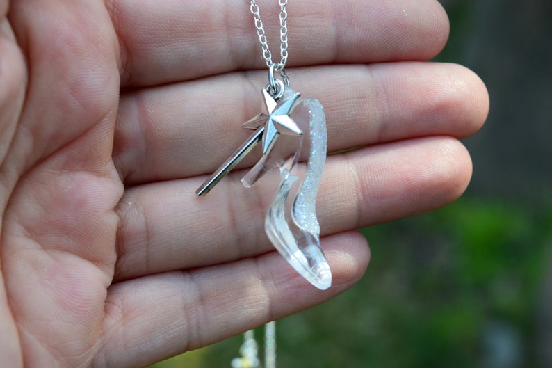 Pu&ograve; includere: Una collana d'argento con un ciondolo a forma di scarpetta di vetro trasparente e un ciondolo a forma di bacchetta magica con una stella d'argento.