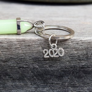 May include: A silver key chain with a green glow-in-the-dark crystal charm and a silver charm with the year 2020.