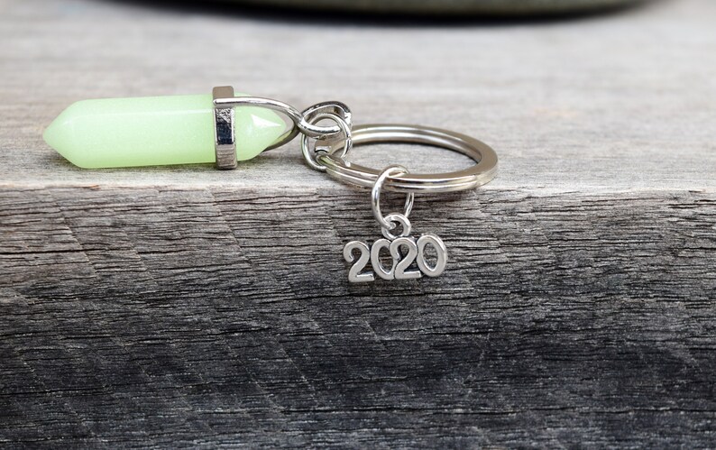 May include: A silver key chain with a green glow-in-the-dark crystal charm and a silver charm with the year 2020.