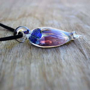 Pu&ograve; includere: Una collana con un ciondolo di vetro con un vortice blu e viola all'interno. Il ciondolo &egrave; attaccato a un cordoncino nero.
