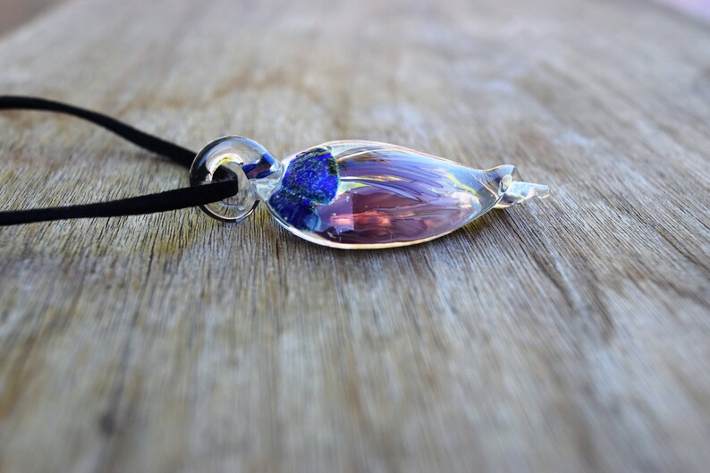 Pu&ograve; includere: Una collana con un ciondolo di vetro con un vortice blu e viola all'interno. Il ciondolo &egrave; attaccato a un cordoncino nero.