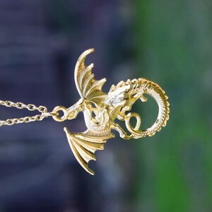May include: A gold dragon pendant necklace. The dragon is curled up with its wings spread out. The necklace is on a chain.