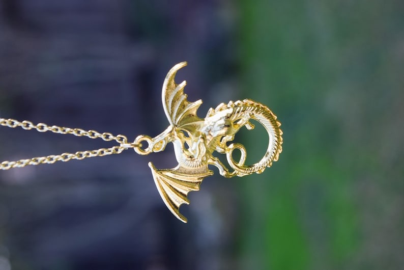 May include: A gold dragon pendant necklace. The dragon is curled up with its wings spread out. The necklace is on a chain.