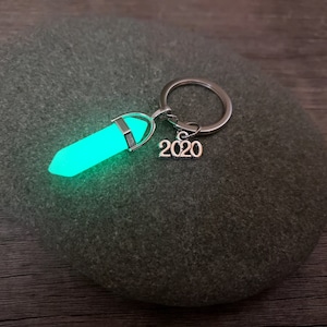 May include: A silver key chain with a glowing green crystal charm and a silver charm with the year 2020.