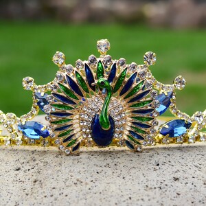 May include: A gold crown with a peacock design. The peacock is made of blue, green, and gold enamel. The crown is decorated with clear and blue rhinestones.