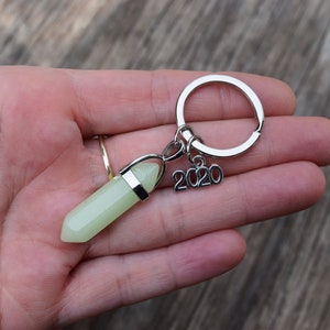 May include: A silver key chain with a green glow-in-the-dark crystal charm and a silver charm with the year 2020.