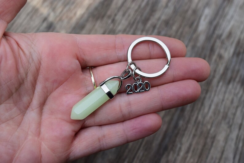 May include: A silver key chain with a green glow-in-the-dark crystal charm and a silver charm with the year 2020.