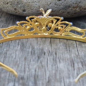 May include: A gold tiara with a delicate design and blue gemstones. The tiara is made of metal and has a simple, elegant style.
