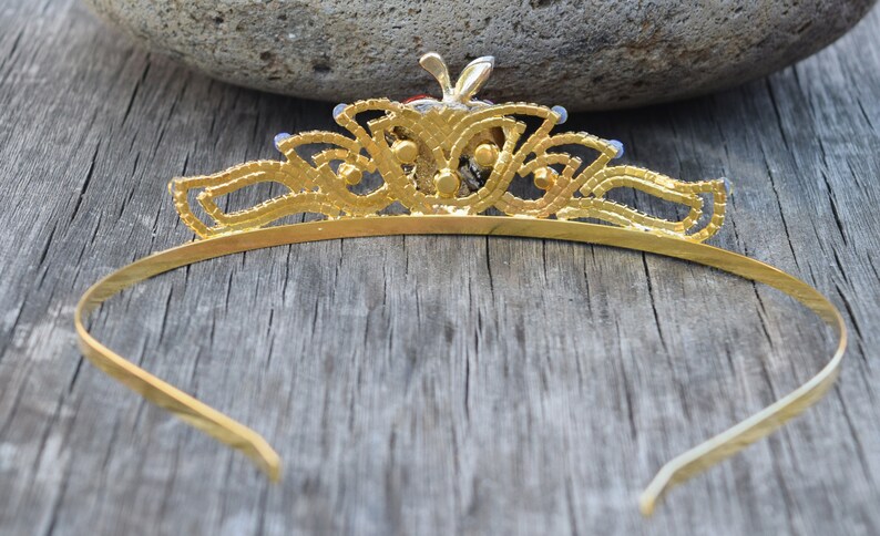 May include: A gold tiara with a delicate design and blue gemstones. The tiara is made of metal and has a simple, elegant style.