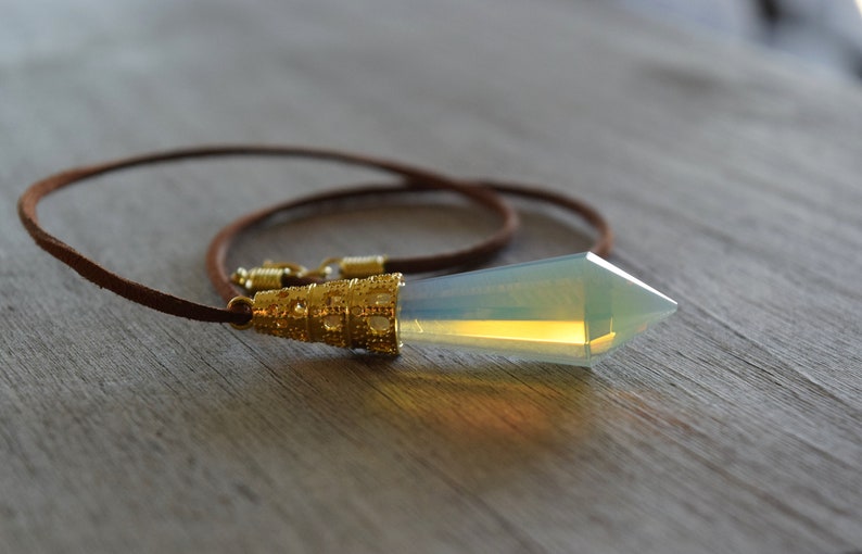 May include: A brown leather cord necklace with a gold-toned pendant featuring a clear, iridescent crystal point.