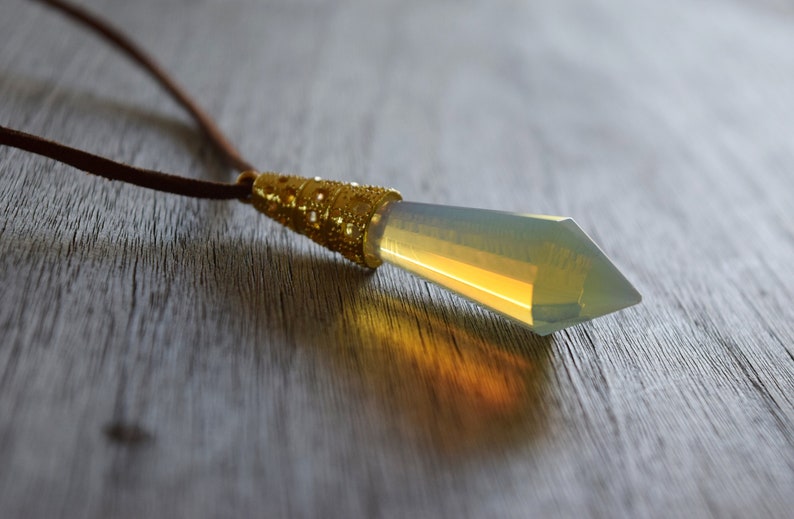 May include: A gold and clear crystal pendant necklace with a brown leather cord. The pendant is shaped like a long, pointed crystal.
