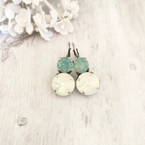 May include: A pair of silver dangle earrings with two clear crystal stones. The top stone is a light blue color and the bottom stone is a white opal color.