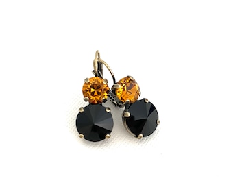 May include: A pair of dangle earrings with black and amber crystal stones. The earrings have a gold tone finish.