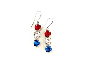 May include: A pair of silver dangle earrings with three red, white, and blue crystal stones.