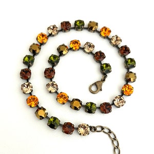 May include: A necklace made of small, faceted glass beads in shades of green, brown, and orange. The beads are connected by a silver chain and the necklace has a lobster clasp closure.