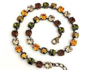 May include: A necklace made of small, faceted glass beads in shades of green, brown, and orange. The beads are connected by a silver chain and the necklace has a lobster clasp closure.