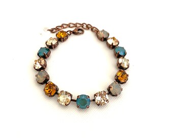 May include: A delicate bracelet featuring a series of round, colorful gemstones in shades of teal, gold, and cream. The stones are set in a bronze-colored metal, creating a vintage-inspired look. The bracelet is designed to fit a wrist.