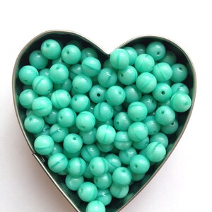 May include: A heart-shaped container filled with turquoise blue round beads with white swirl designs.