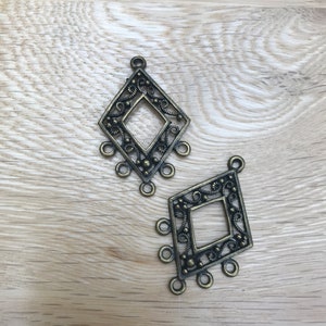 May include: Two antique gold-toned metal diamond-shaped charms with intricate filigree designs and five loops on each charm.