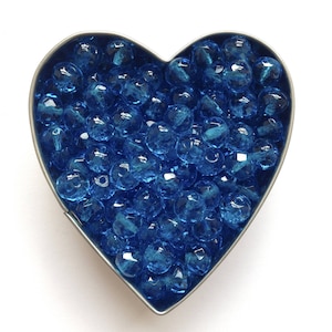 May include: A heart-shaped metal container filled with bright blue glass beads.