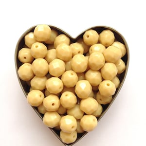 May include: A heart-shaped container filled with a large quantity of cream-coloured faceted glass beads.