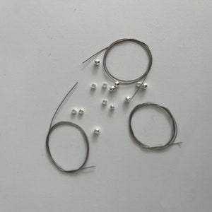 May include: A set of silver beads and wire for jewelry making. The beads are small and round, and the wire is thin and flexible.