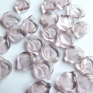 May include: A collection of translucent, pale pink glass beads with a slightly iridescent finish. The beads are shaped like petals and have a delicate, feminine look.