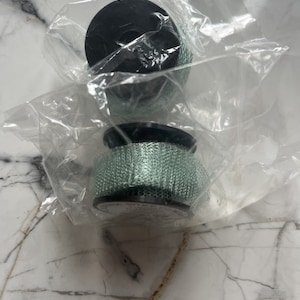 May include: Two black and green mesh filters, packaged in clear plastic. The filters have a cylindrical shape with a black top and bottom. The mesh is a light green color.