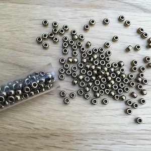 May include: A close-up of a clear plastic tube filled with small, round, gold-coloured beads. The beads are scattered on a light brown wooden surface.