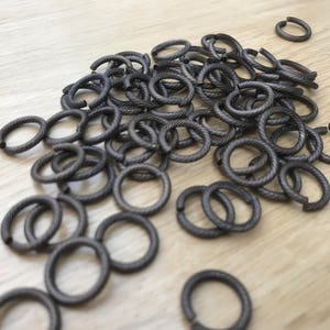 May include: A large pile of black metal jump rings. The rings are all the same size and are arranged in a random pattern.
