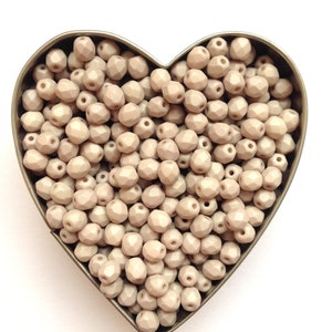 May include: A heart-shaped container filled with light beige faceted glass beads.