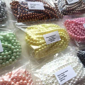 May include: Assortment of glass pearl beads in various colours, including pastel green, pastel yellow, bright white, copper, black, and pink. Each bag contains 600 pieces of 6mm beads.