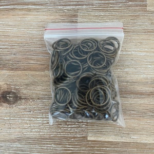 May include: A clear plastic bag filled with a large quantity of small, gold-colored metal jump rings.