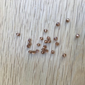 May include: A scattering of small, gold-coloured, metallic beads on a light wood surface.