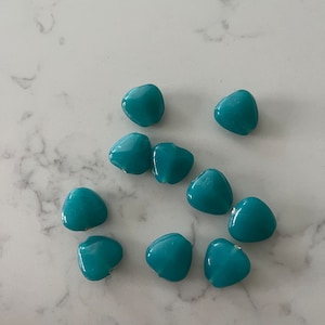 May include: Ten teal blue heart-shaped glass beads. The beads are smooth and glossy.