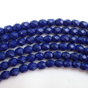 May include: A strand of cobalt blue faceted glass beads. The beads are round and have a textured surface.
