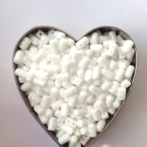 May include: A heart-shaped container filled with white, opaque, rectangular beads with two holes in each bead.
