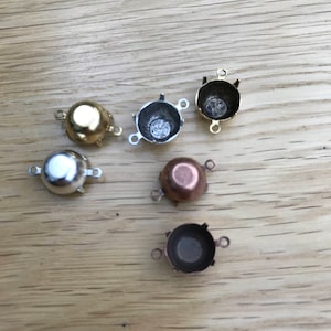May include: Five metal settings for jewellery making. The settings are in different finishes: gold, silver, and copper. Each setting has three prongs and a round cup.